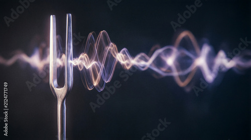 Tuning fork vibrating with luminous sound waves floating in a dark void
