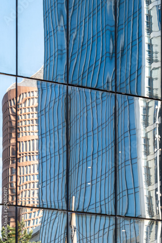 Within the frame, a tower bends inside a blue reflection on glass, while the facade and vertical windows stretch the building until architecture becomes controlled distortion.