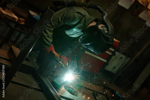 Fotografía Young adult Caucasian male welder in protective mask welding metal in workshop, creating bright sparks
