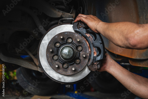Auto mechanic installing car front brake caliper and brake pads.
