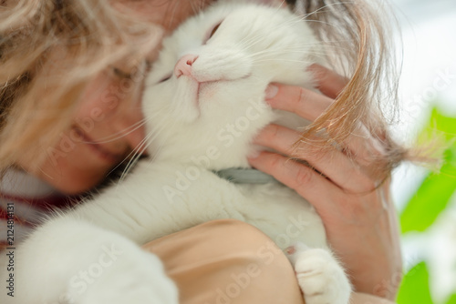 A loving woman holds her white cat close, pressing faces together in a tender embrace. This pet owner shares a serene, affectionate moment indoors, creating a cozy atmosphere of pure comfort and love.