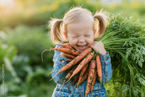  joyous blonde toddler girl with pigtails standing in a lush organic vegetable garden,