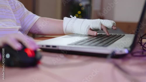 Child with casted arm using laptop keyboard. Computer dependence and teen gaming during injury treatment. Remote learning and education during outpatient recovery.