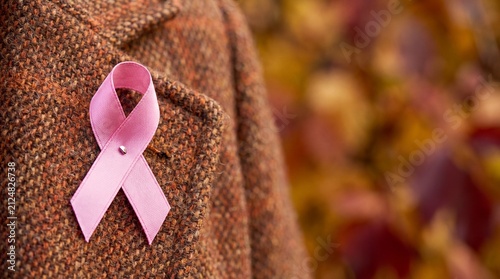 Pink Ribbon Symbolizing Breast Cancer Awareness on a Brown Coat Against a Colorful Autumn Background, copy space