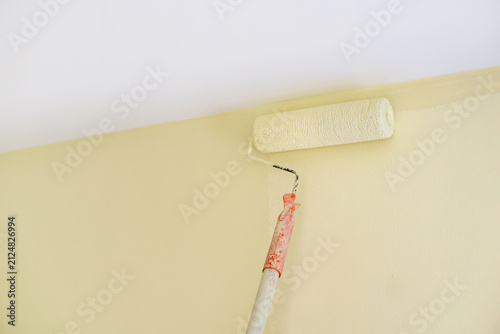 A paint roller is being used to apply color of  cream paint on the wall of a newly renovated room. The wall have a smooth finish, indicating recent update.