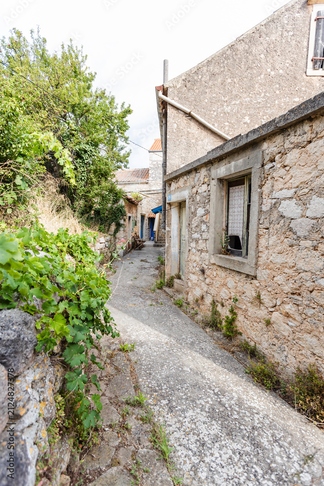 Fototapeta premium Picturesque Croatian Mediterranean island village featuring traditional stone houses with weathered facades, narrow cobblestone alley, and rustic architecture.