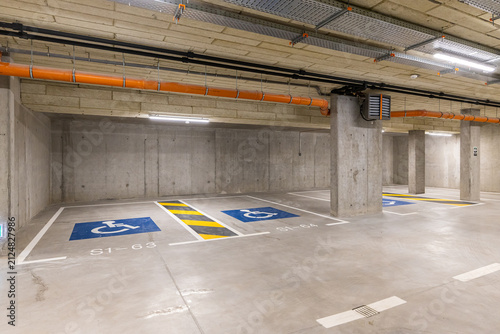 Modern underground concrete parking garage featuring designated handicap accessible spaces marked with blue wheelchair symbols and safety floor lines under bright ceiling lights
