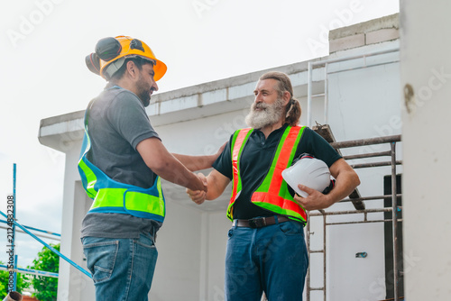Two construction workers shaking hands closing a deal with agreement at house building site