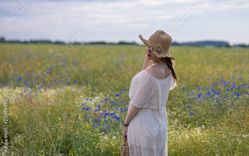 Fotografie Woman Looking into the Distance in a White Dress and Straw Hat