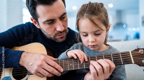 A loving father teaching his young daughter how to play the acoustic guitar at home