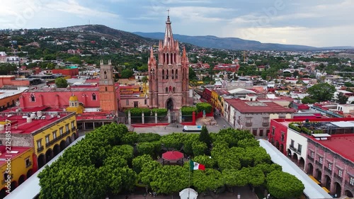 A breathtaking aerial panorama capturing the soaring neo-Gothic spires of the Parroquia de San Miguel Arcángel rising above the historic colonial cityscape.