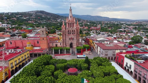 A cinematic aerial perspective capturing the striking neo-Gothic facade and soaring masonry of the historic Parroquia de San Miguel Arcángel.
