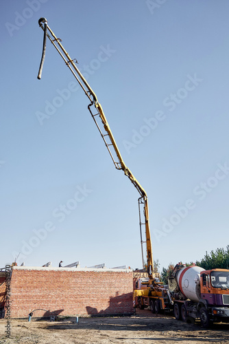 Fotografía Vertical low angle view of a yellow concrete pump truck with extended placing boom operating next to a concrete mixer truck at a house construction site