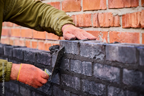 Принти на полотні Close-up of a mason using a trowel to adjust wet cement mortar while placing dark clinker bricks along a blue alignment string line