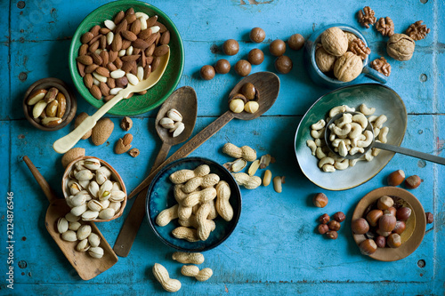 Overhead view of various nuts in bowls and on spoons on blue rustic table