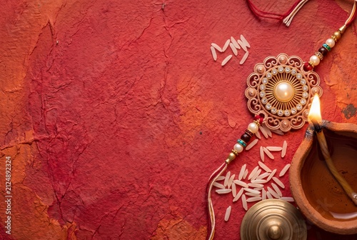Raksha bandhan festival background with a decorative rakhi, diya lamp and rice grains on textured red paper