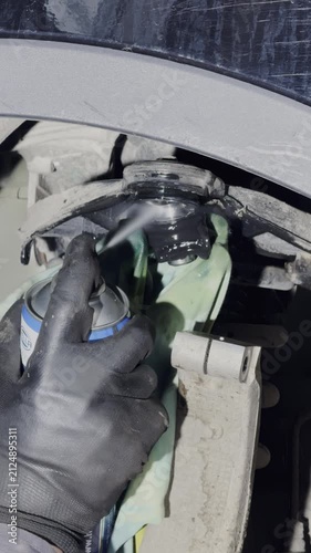 Technician uses aerosol spray to clean car suspension part. Mechanic applies cleaner to ball joint removing residual dirt on surface of component
