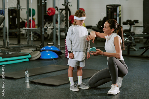 Photography Female Caucasian trainer instructing Caucasian child in gym while holding smartphone