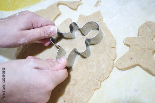Child's hands using a gingerbread man cookie cutter to shape dough for baking