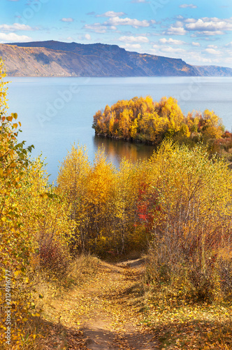 Autumn landscape of Baikal Lake. Footpath with yellow fallen leaves to Cape Shamansky - natural attraction on September sunny windy day. Nature background. Outdoor activities, hiking and travel