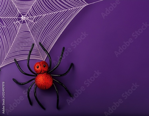 Close-up of big red and black spiders decoration on a web on dark purple background with copy sapce