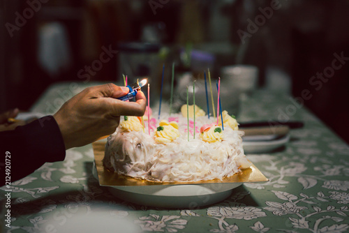 Close up of hand using a lighter to light candles on white coconut birthday cake.