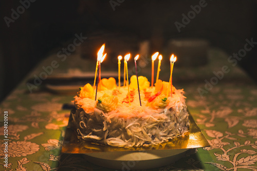 Birthday cake covered in shredded coconut and brightly glowing lit candles in a dark.