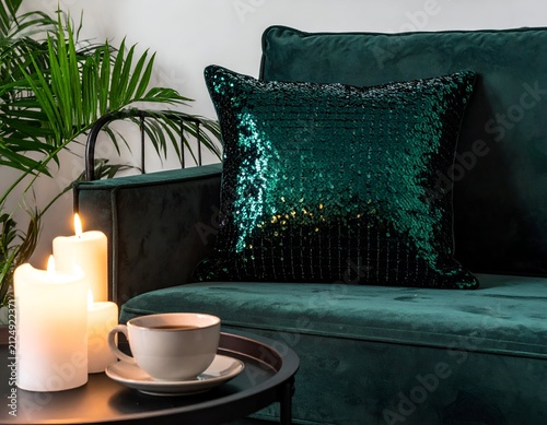 Cozy scene sequined pillow on a green couch, candles, coffee, and a plant