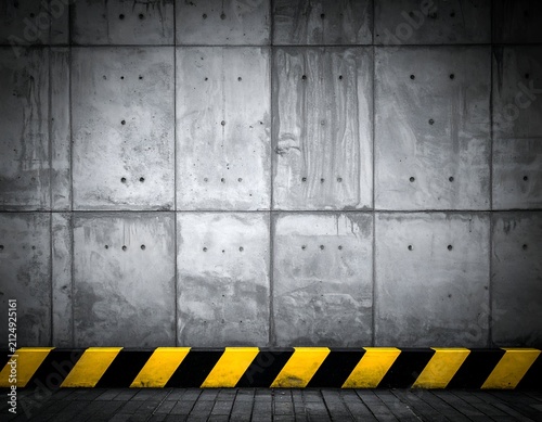 Grey concrete wall with black/yellow caution strip on a dark floor