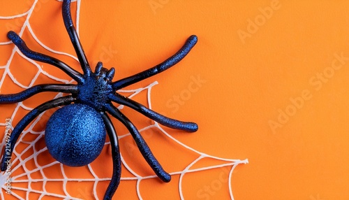 Close-up of big blue and black spiders decoration on a web on orange background with copy space. Halloween concept