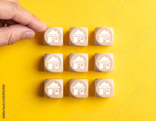 Hand places cube with house icon among others, arranged in grid on yellow background