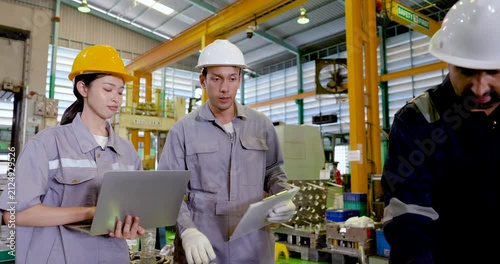 Asian female technician holds laptop beside two adult male engineers, reviewing production record and checklist for workflow planning, inspection tracking and teamwork in slow motion