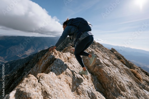 Hiker scrambling along a jagged mountain ridge with backpack and trekking shoes for outdoor adventure banner and travel background