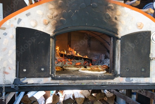 Traditional wood fired pizza oven with fireplace and stoked firewood.