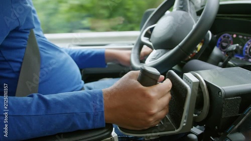 Driver with a physical impairment using assistive technology on a car dashboard and adaptive hand controls for safe and comfortable driving.