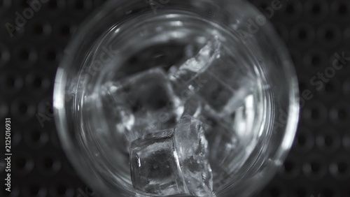 Foto Clear glass with ice cubes filling up on dark bar surface, showing refreshing co