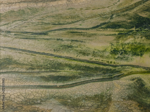 Aerial view of cracked mudflats and mossy terrain on Aestian Island, featuring intricate patterns of dry earth and green vegetation in Krynica Morska, Pomeranian Voivodeship, Poland.
