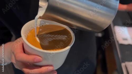 Barista pouring milk for double rosette and hummingbird latte art in white ceramic mug