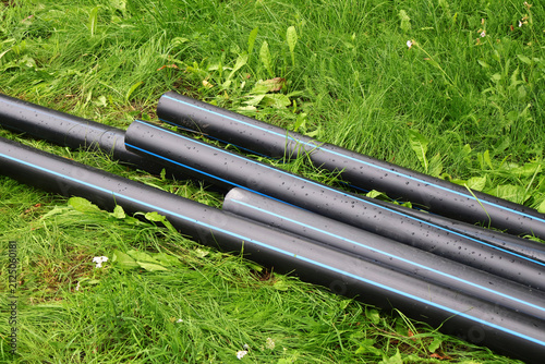 Plastic pipes on the grass. A pile of gray water pipes lies on the ground, pipes in the yard.