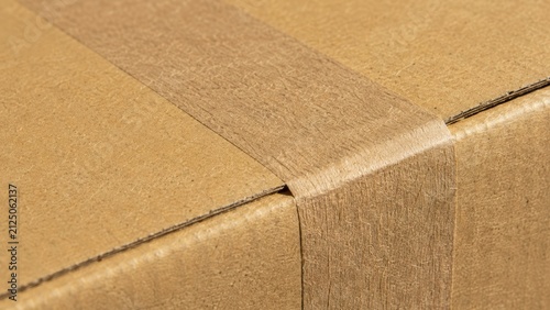 Cardboard box sealed with brown paper tape for delivery background closeup