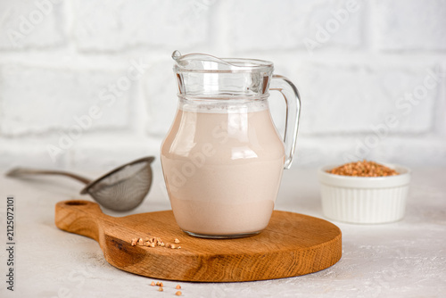 Homemade green buckwheat milk in glass with raw buckwheat grains, healthy vegan dairy-free drink