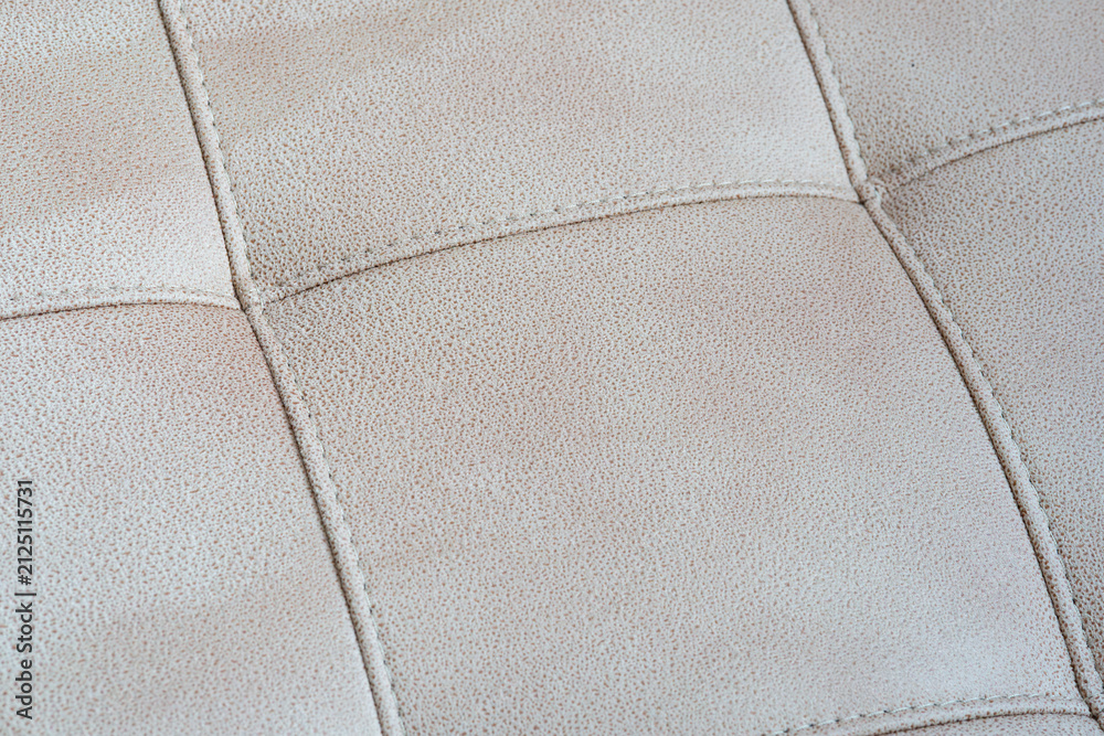 Obraz premium Close-up of a beige tufted leather upholstery texture with stitched crossed seams