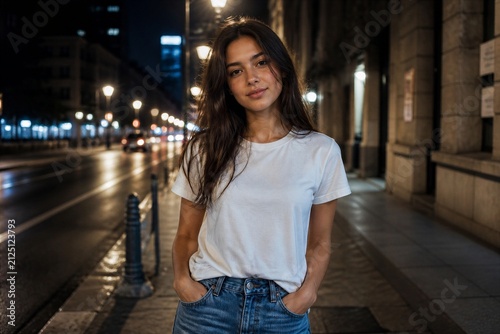 Young woman standing hands in pockets on city street at night