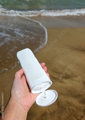 White sunscreen tube on golden beach sand near the ocean waves. High quality photo