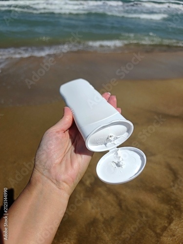 White sunscreen tube on golden beach sand near the ocean waves. High quality photo