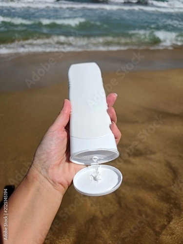 White sunscreen tube on golden beach sand near the ocean waves. High quality photo