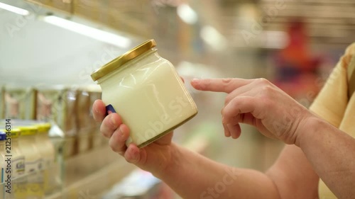 Customer reading label on jar of fermented milk product in supermarket close-up