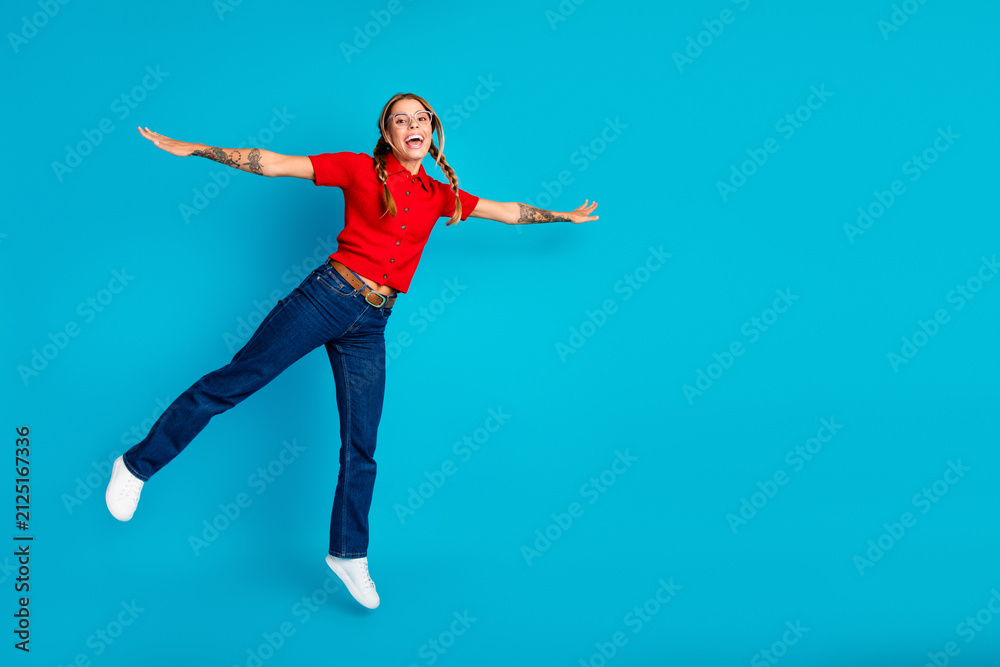 Fototapeta premium Adorable young woman jumping with joy in a red polo shirt against a blue background for lifestyle fashion and advertising