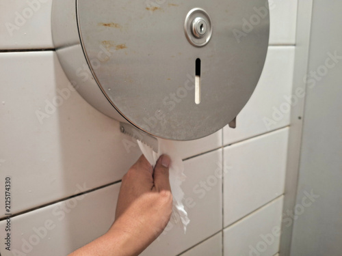 Foto closeup of left hand pulling tissue from tissue dispenser in toilet