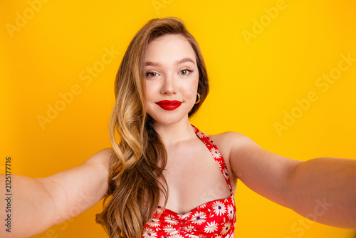 Cuadro en lienzo Young woman taking a selfie smiling in a red floral dress against a bright yello